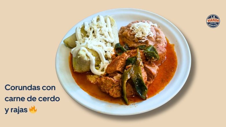 Plate of corundas with pork and rajas in a red sauce, topped with cheese, on a beige background; La Vianda logo in the corner. Caption reads 'Corundas con carne de cerdo y rajas'.
